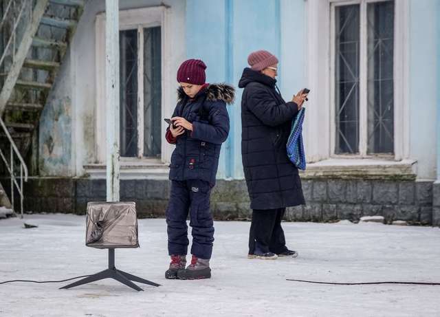 Місцеві жителі користуються терміналом Starlink під час російської атаки на Часів Яр у Донецькій області України 31 січня